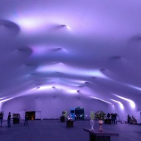 Envelopamento total em malha tensionada branca, espaço de 1.850m² com iluminação cênica.